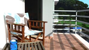 A wooden table and chairs on a balcony with a view of a green landscape and a building in the distance. - Sesimbra Holiday Apartment (Sesimbra)