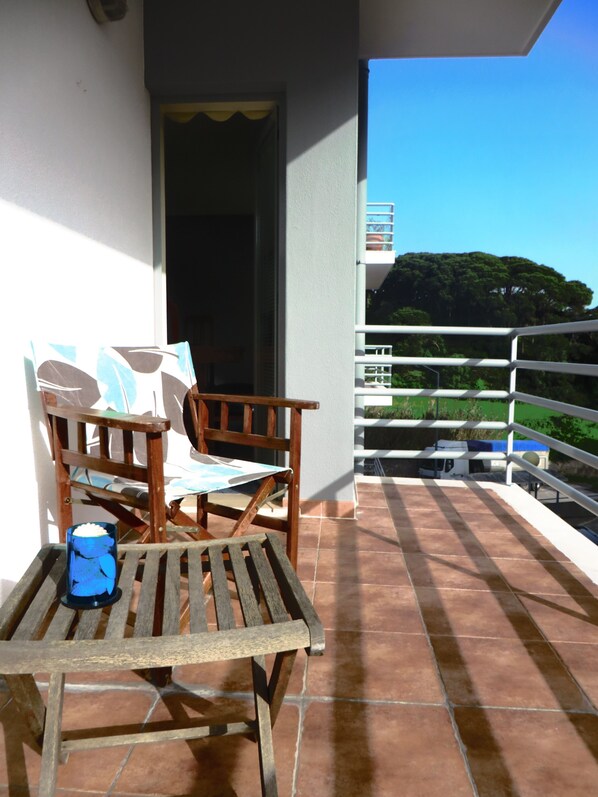 A wooden table and chairs on a balcony with a view of a green landscape and a building in the distance.