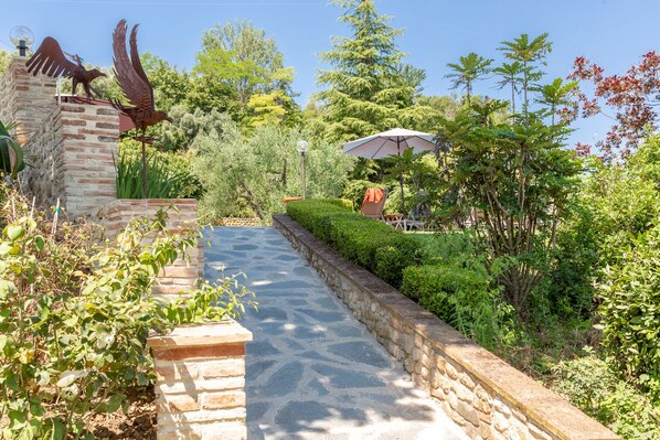 A stone pathway leading through a lush garden with a statue of birds on a pillar, surrounded by greenery and a clear sky. - 1600s Rural Villa in Chianti with Pool and AC just a few steps from Florence (Montespertoli)