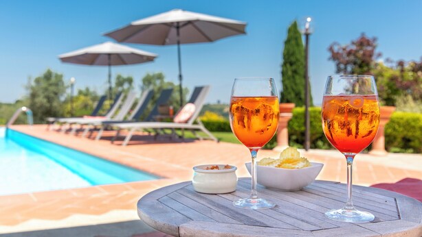 A poolside table with two glasses of red drink, a bowl of chips, and a small dish of dip, with a pool and lounge chairs in the background. - 1600s Rural Villa in Chianti with Pool and AC just a few steps from Florence (Montespertoli)