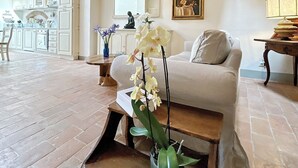 A spacious living area with a chandelier, a sofa, a coffee table with flowers, a painting, and a kitchen in the background. - 1600s Rural Villa in Chianti with Pool and AC just a few steps from Florence (Montespertoli)
