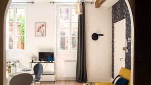 Ein modernes Wohnzimmer mit einem gelben Sofa, einem Esstisch mit Stühlen, einem Fernseher und einem großen Fenster mit Vorhängen.
