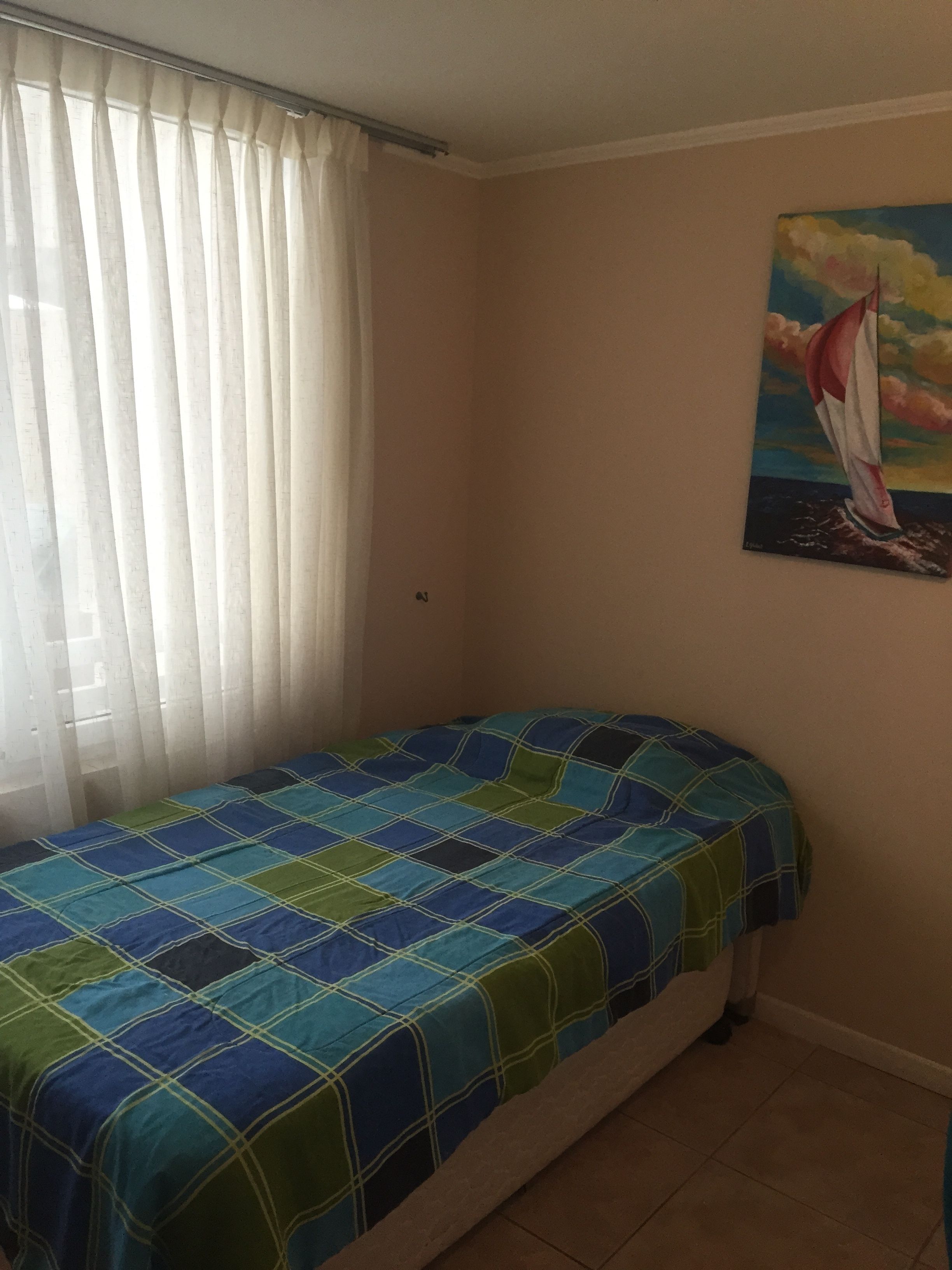 A bedroom with a bed, a window with curtains, and a painting on the wall.