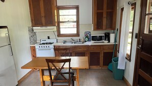 A kitchen with wooden cabinets, a white stove, a microwave, and a sink. - Monthly Lakeside Retreat Cabin (Danbury)