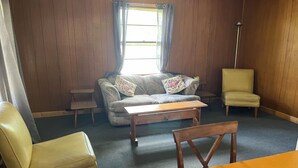 A living room with a sofa, a chair, a small table, and a window with curtains. - Monthly Lakeside Retreat Cabin (Danbury)