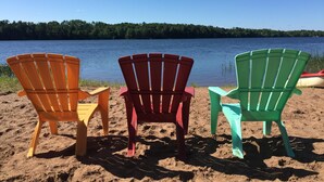 Three colorful Adirondack chairs facing a calm lake with a forested shoreline. - Monthly Lakeside Retreat Cabin (Danbury)