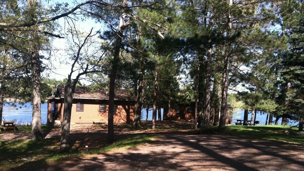 A cabin by a lake with a dirt path leading to it, surrounded by trees. - Monthly Lakeside Retreat Cabin (Danbury)
