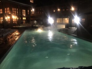 Ein Hallenbad mit klarem Wasser, umgeben von einem Gebäude mit vielen Fenstern und Beleuchtung.