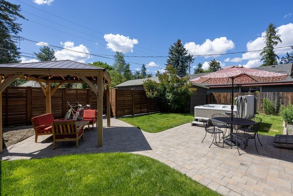Un cortile con una pergola in legno, una vasca idromassaggio e un tavolo da esterno con sedie.