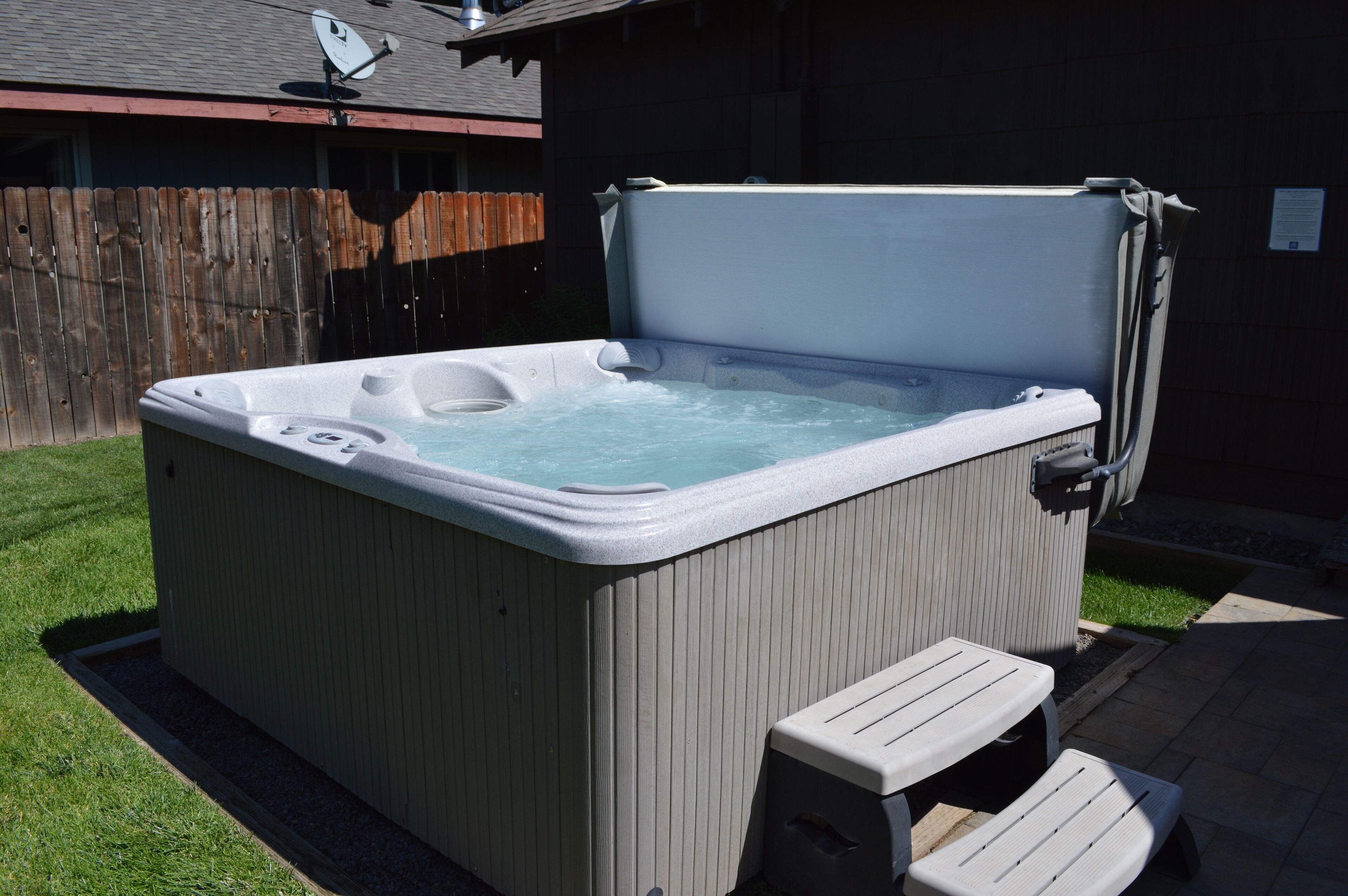 A hot tub with steps and a cover, surrounded by a wooden fence and a grassy yard.