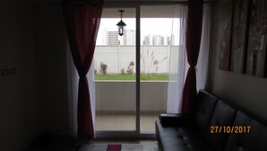 A living room with a sliding glass door leading to a balcony. There is a black leather sofa and a hanging light fixture. - 52.- HNA Capri (La Serena)
