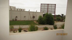 A view of a building with a large billboard, a paved area with plants, and a grassy lawn. - 52.- HNA Capri (La Serena)