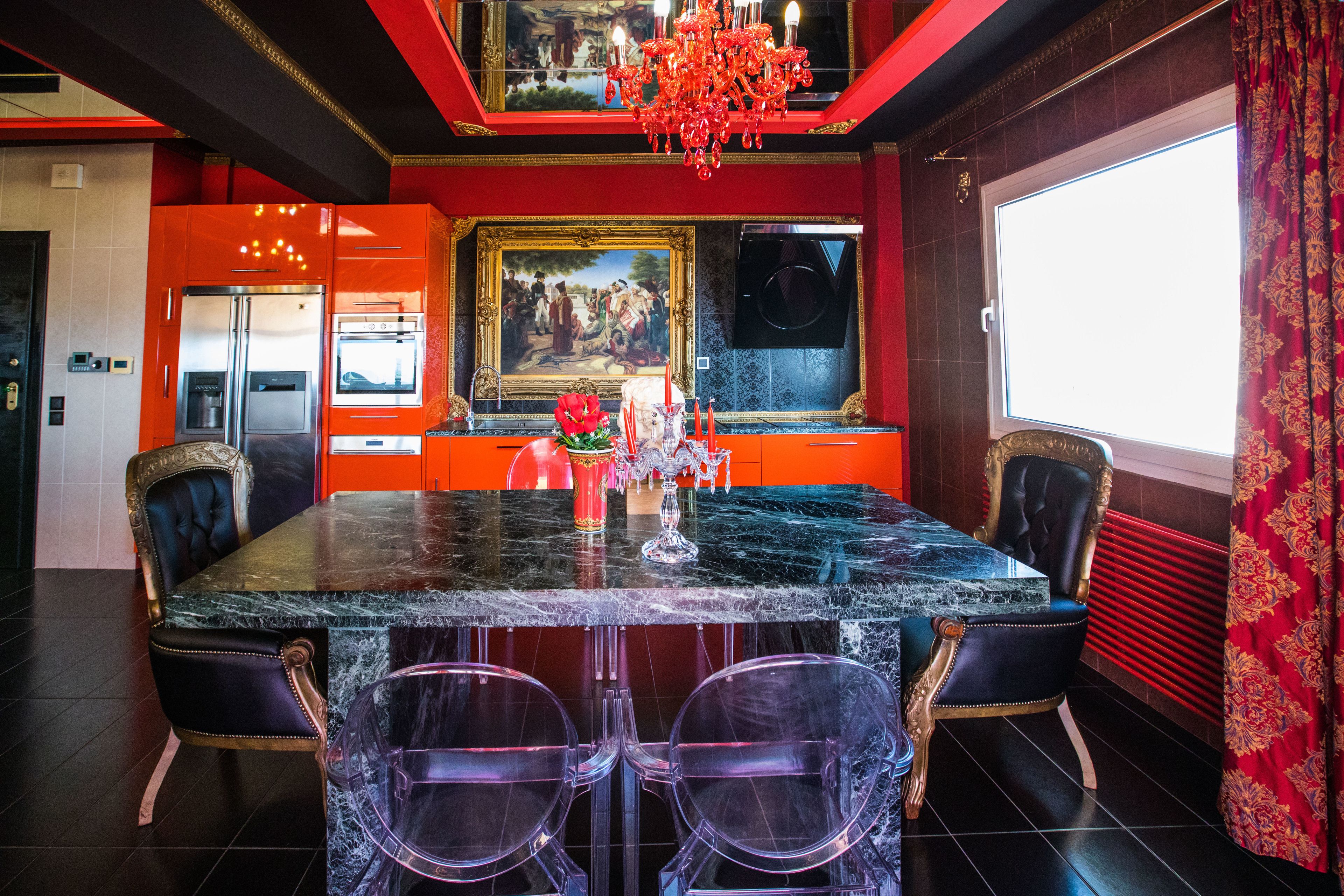A dining area with a marble table, two chairs, a chandelier, and a painting on the wall.