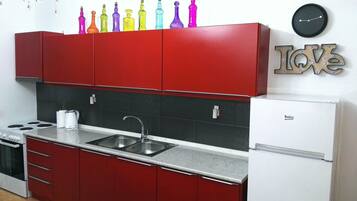 A kitchen with red cabinets, a white refrigerator, a sink, and a clock on the wall.