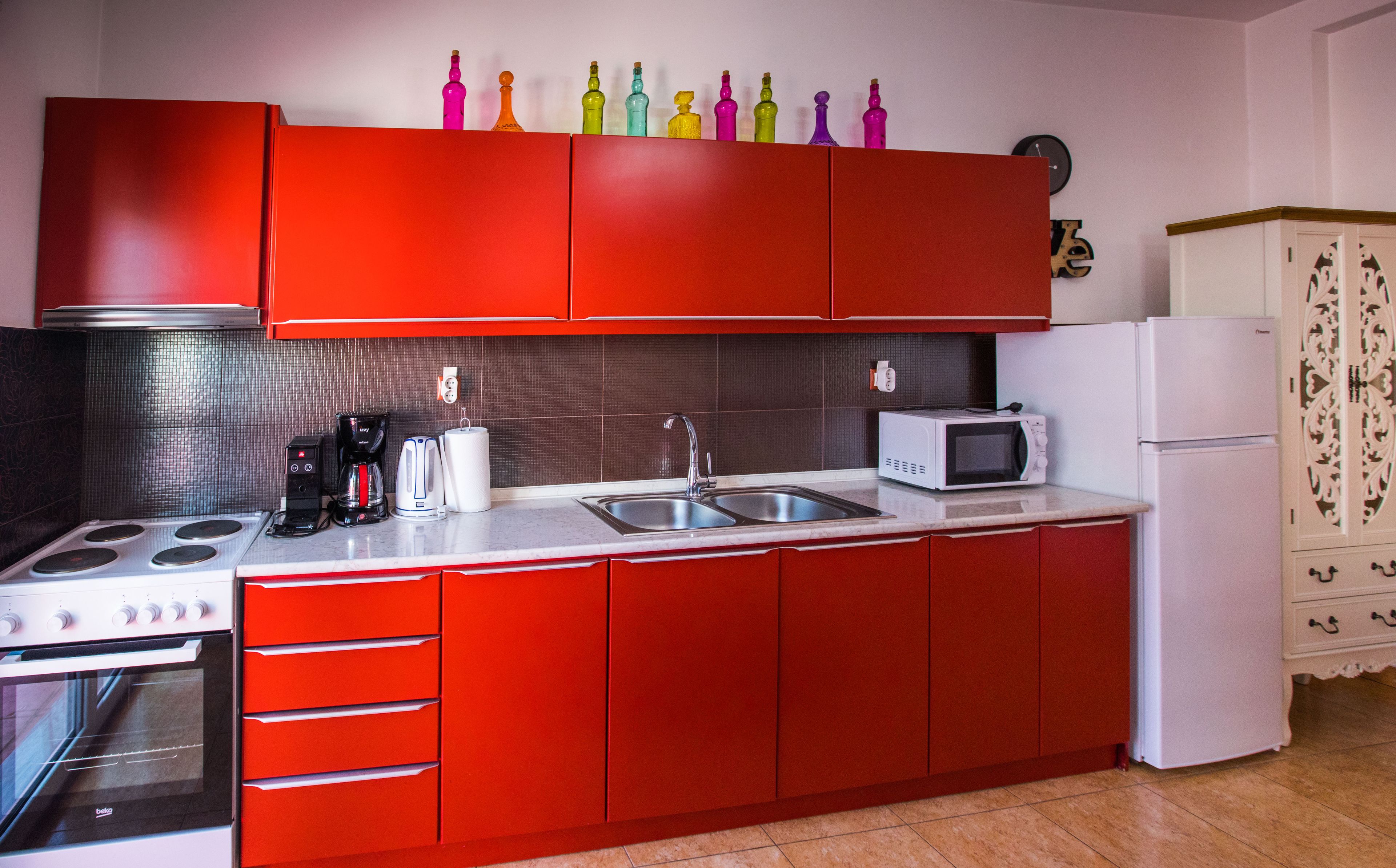 Una cocina con armarios rojos, un refrigerador blanco, un microondas, un fregadero y una estufa.