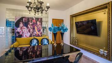 Un comedor con mesa de vidrio, sofá amarillo, centro de mesa floral azul y un espejo grande con marco.