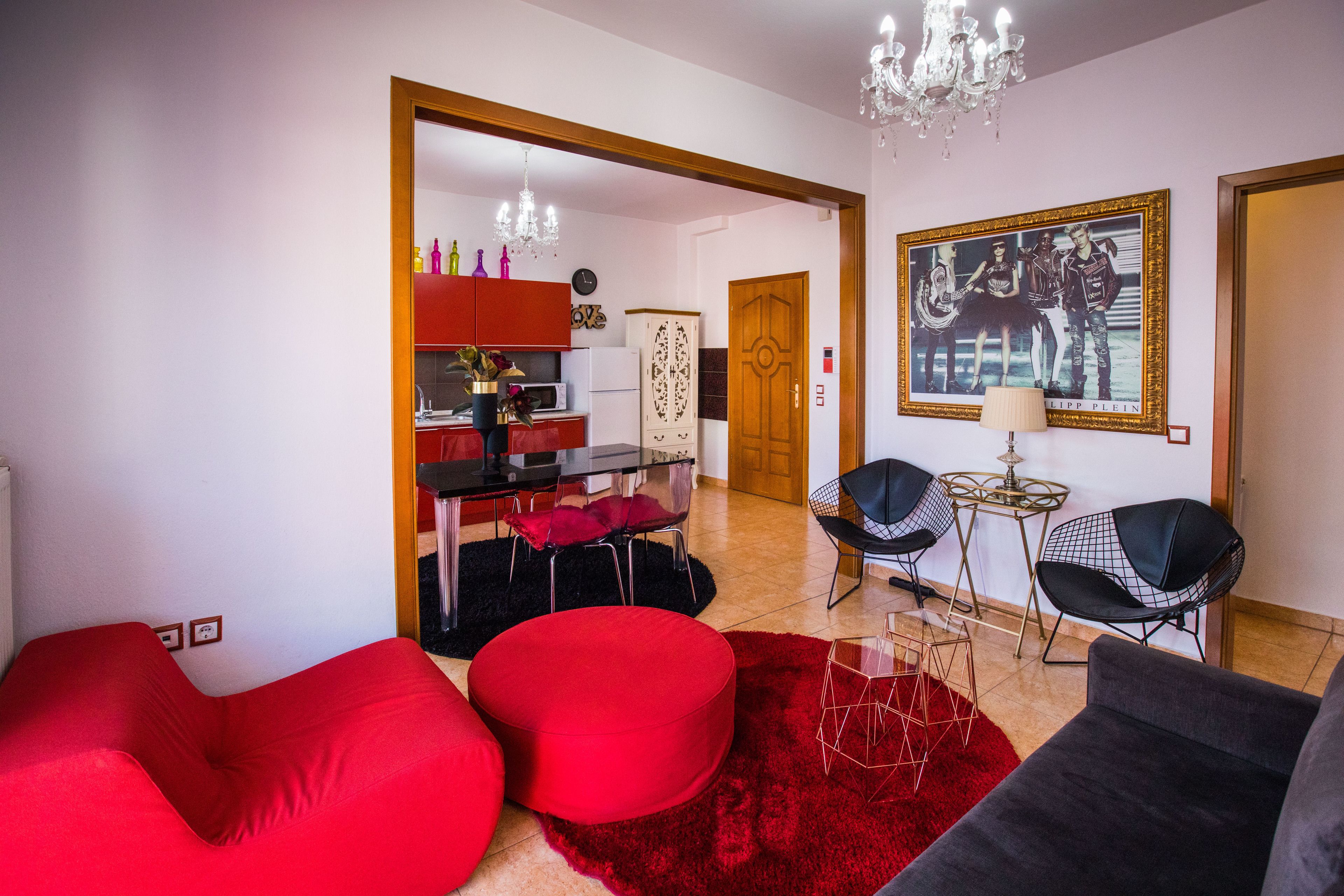 Un salon moderne avec des meubles rouges et noirs, un coin repas avec un buffet rouge et un réfrigérateur blanc, et un lustre.