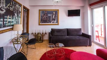 A living room with a dark grey sofa, a red rug, and a chandelier. There are two hexagonal tables with metal frames and a lamp on a small table.
