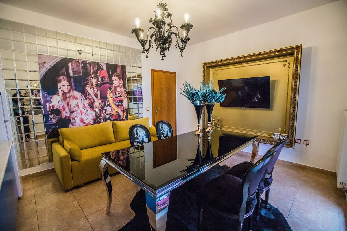 A dining area with a glass table, yellow sofa, and a chandelier.