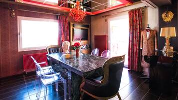 A dining area with a marble table, clear chairs, a chandelier, and a red curtain.