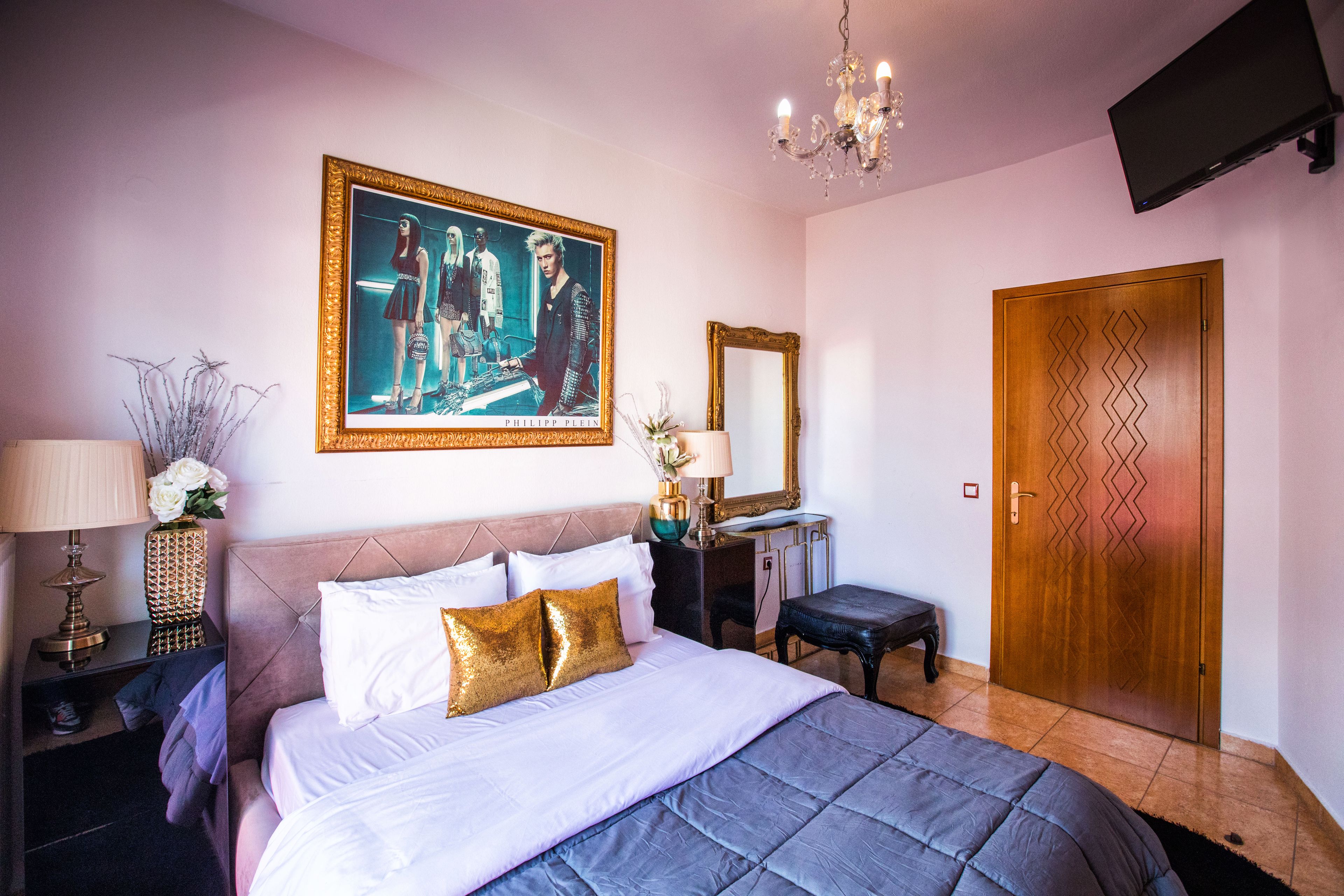 A bedroom with a large bed, a dresser, a vanity with a mirror, a chandelier, and a door with a geometric pattern.