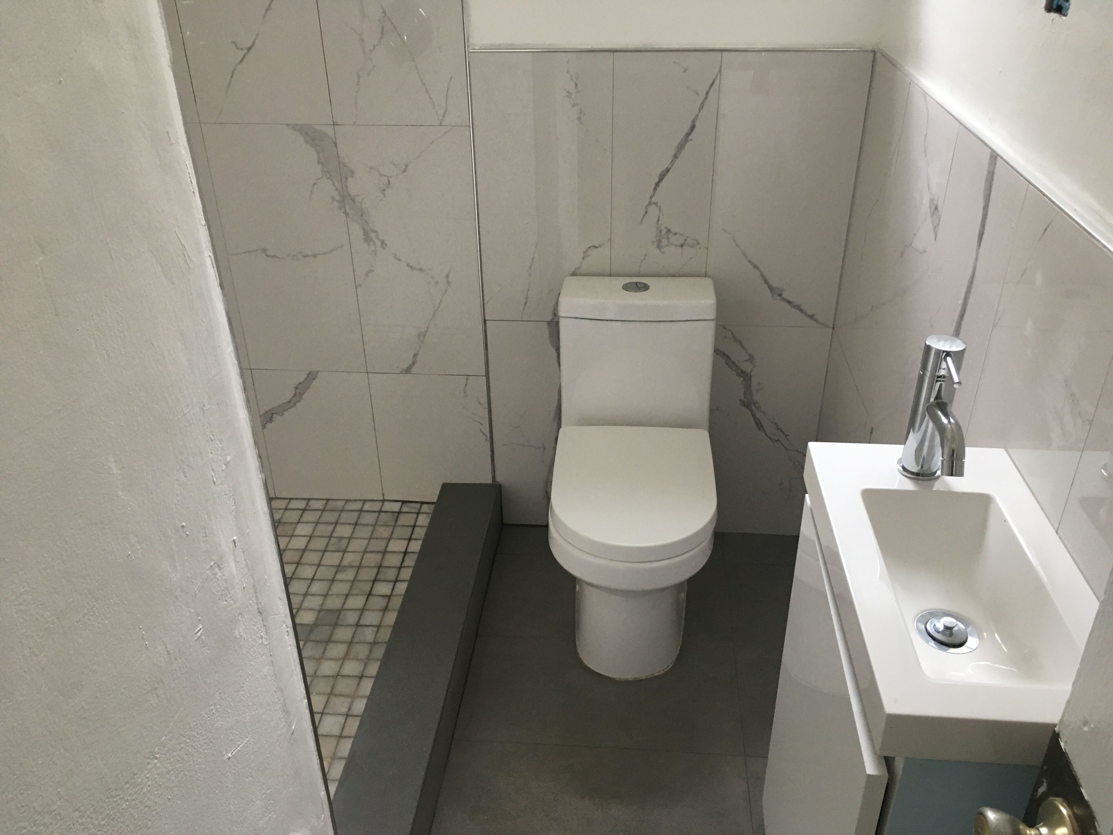 A small, modern bathroom with a toilet, sink, and tiled walls.