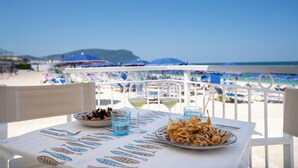 A table with seafood dishes, glasses, and cutlery, overlooking a beach with umbrellas and chairs.