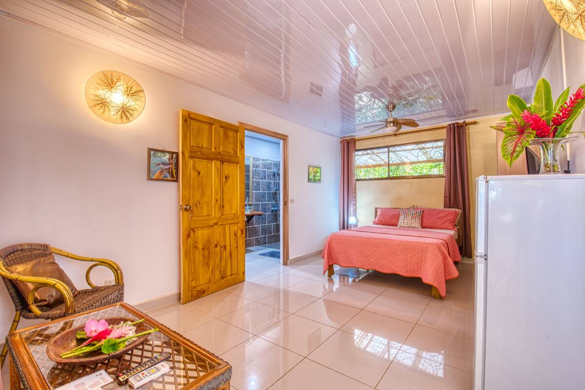 A bedroom with a bed, a wooden door, a ceiling fan, and a window with curtains.
