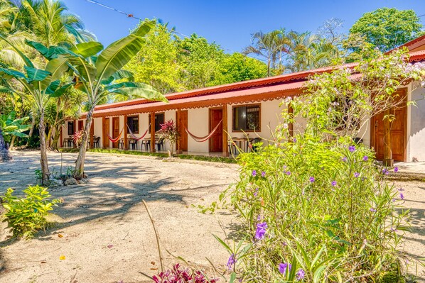 Ein bungalowähnliches Gebäude mit rotem Dach und beigen Wänden, umgeben von üppigem Grün und blühenden Pflanzen.