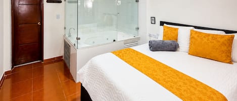 Habitación de hotel con una cama grande, ducha envuelta en vidrio y puerta de madera.