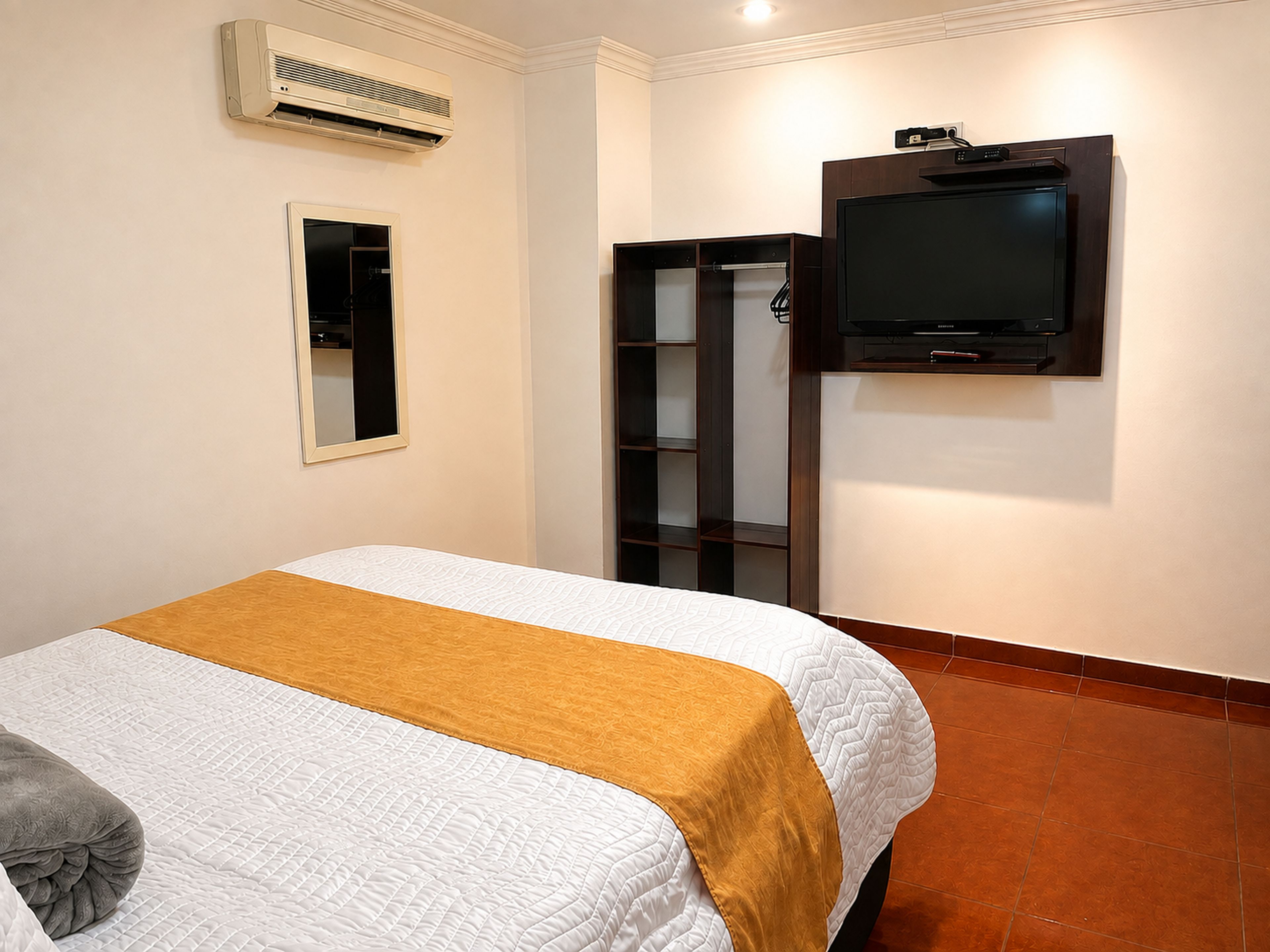 Una habitación de hotel con una cama, un televisor montado en la pared y un armario.