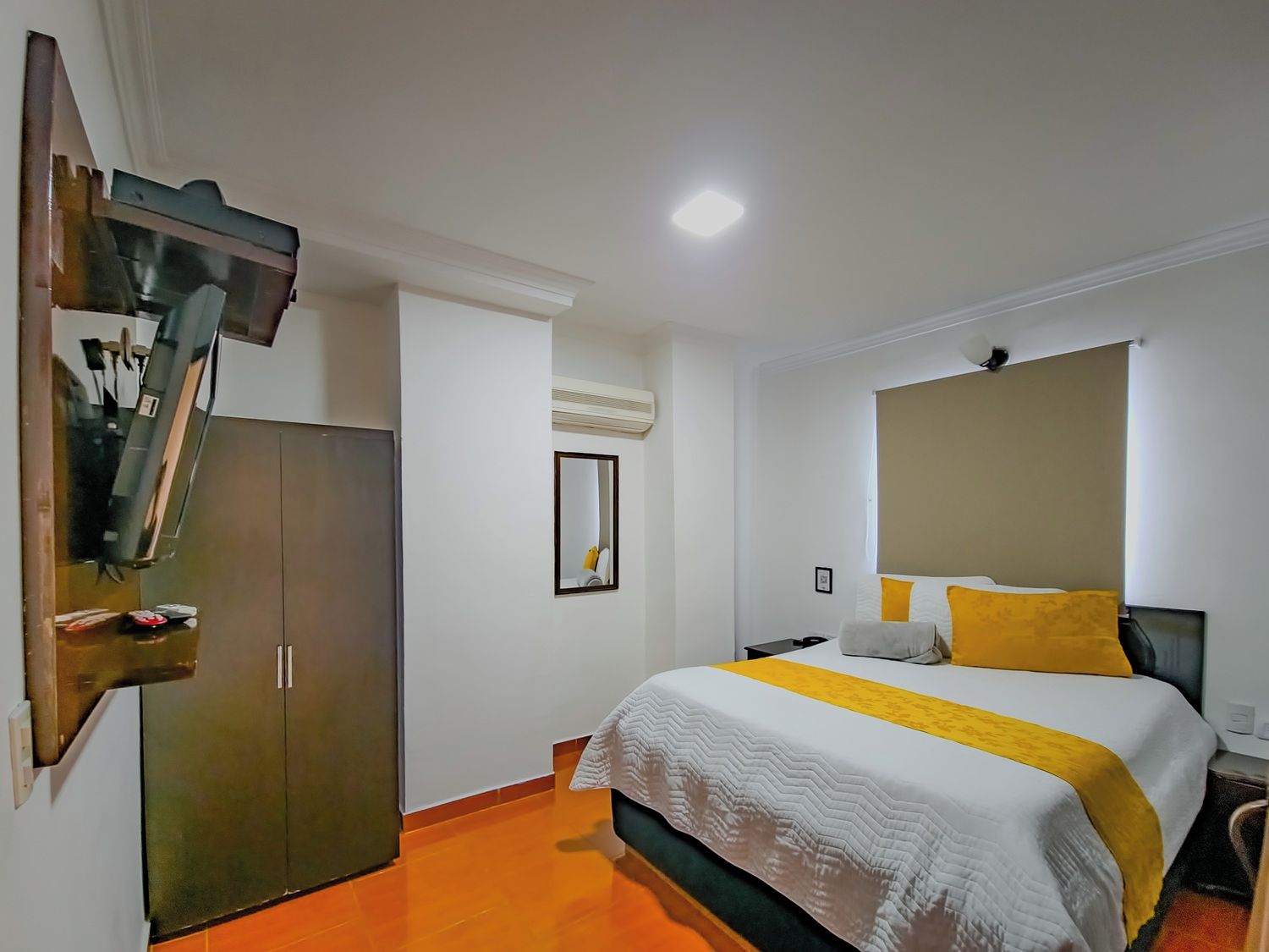 Una habitación de hotel con cama, armario, espejo y mesita de noche.