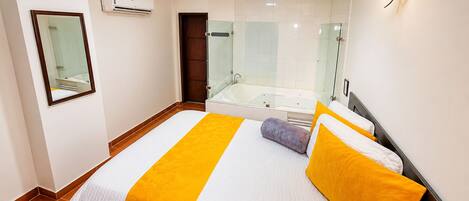 Una habitación de hotel con una cama, un baño con bañera y un espejo en la pared.