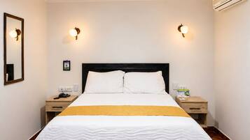 Habitación de hotel con cama, dos mesitas de noche, un tocador, un espejo e iluminación en la pared.