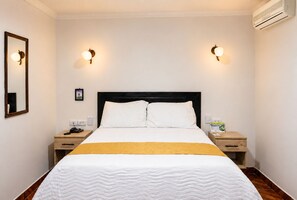 Habitación de hotel con cama, dos mesitas de noche, un tocador, un espejo e iluminación en la pared.