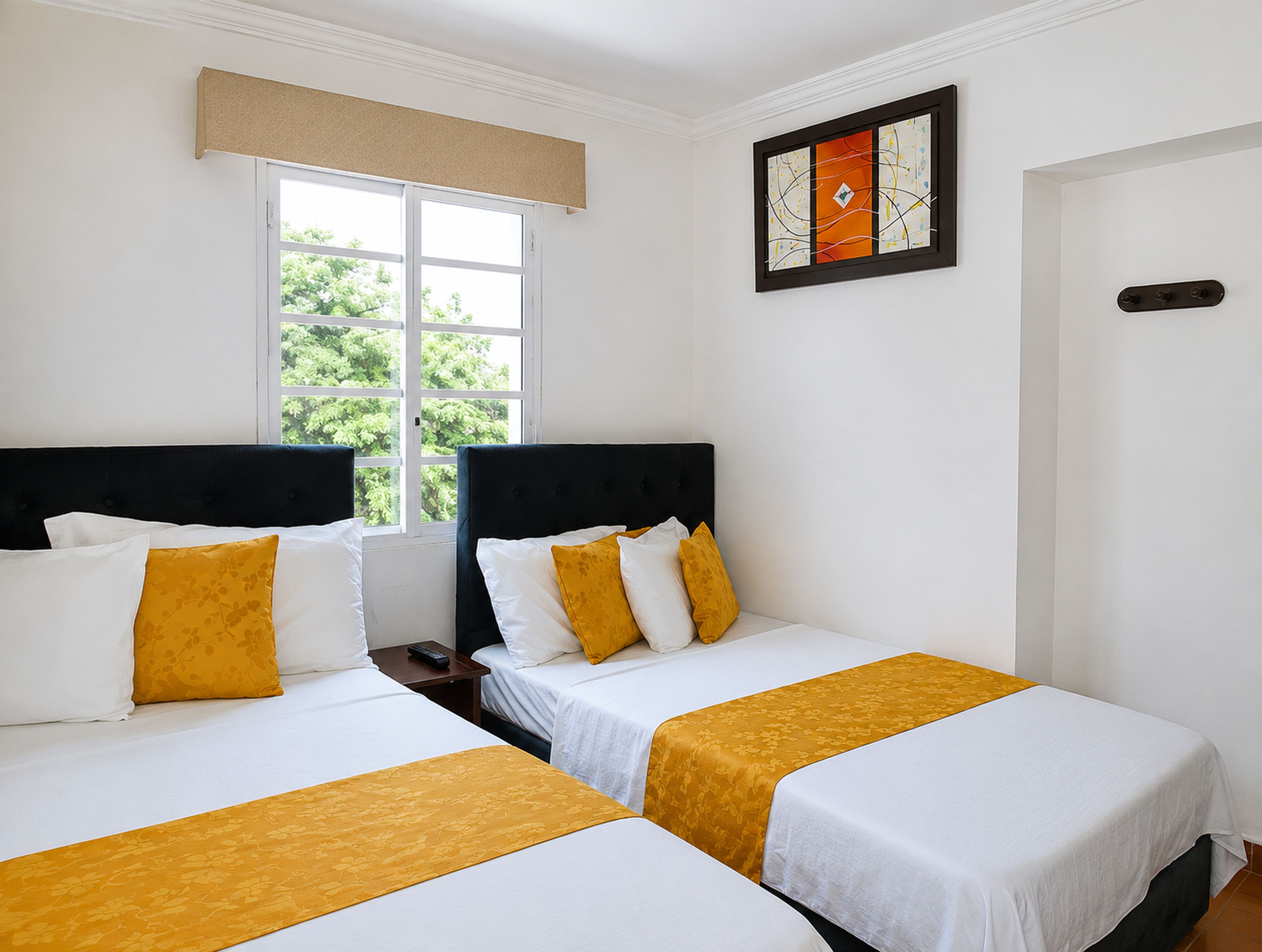 Habitación de hotel con dos camas, una ventana con vista a follaje, una obra de arte enmarcada en la pared y una puerta.