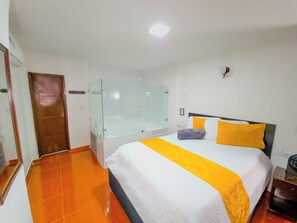 A hotel room with a bed, a glass-enclosed shower, and a door. - Hotel Avenida 3 Real (Cali)