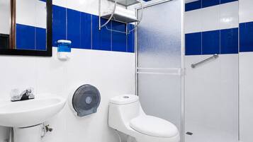 Un baño con lavamanos blanco, inodoro y cabina de ducha con mampara de vidrio.