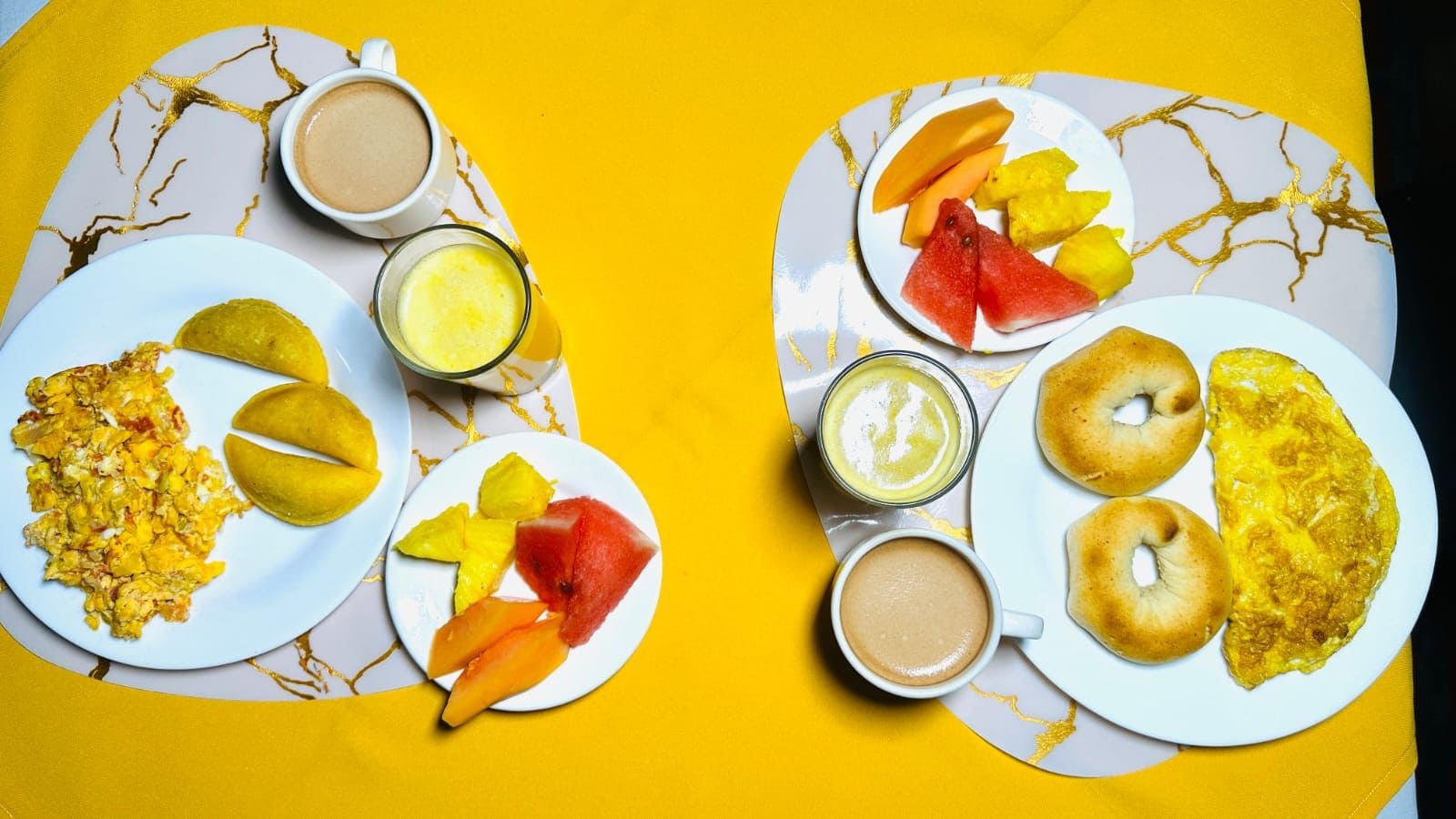 A breakfast setup with scrambled eggs, mango slices, and a plate of bagels.