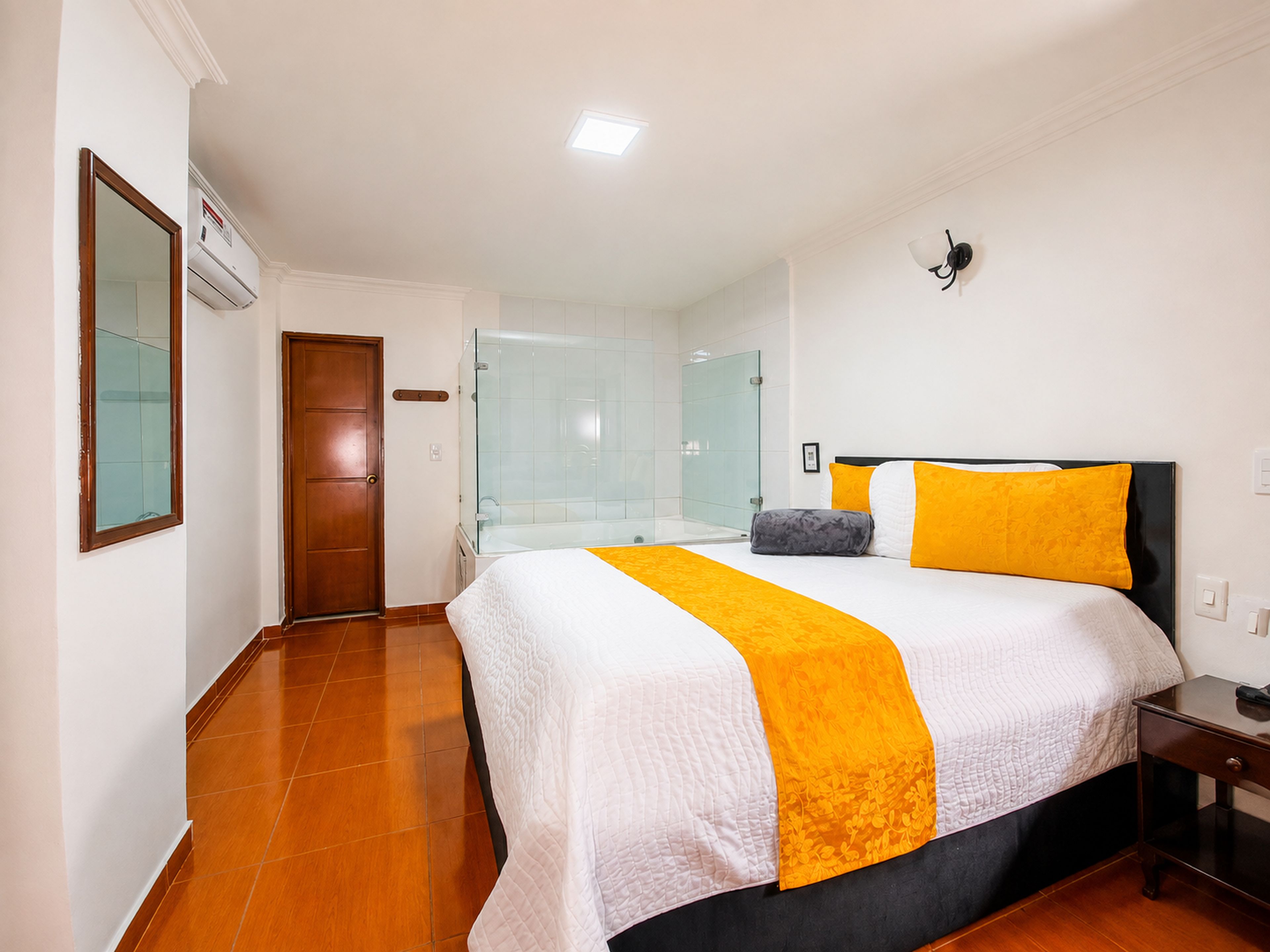 Una habitación de hotel con cama, mesita de noche, espejo, puerta y zona de ducha.