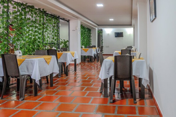 A restaurant with tables covered in white tablecloths and chairs with yellow sashes. - Hotel Avenida 3 Real (Cali)