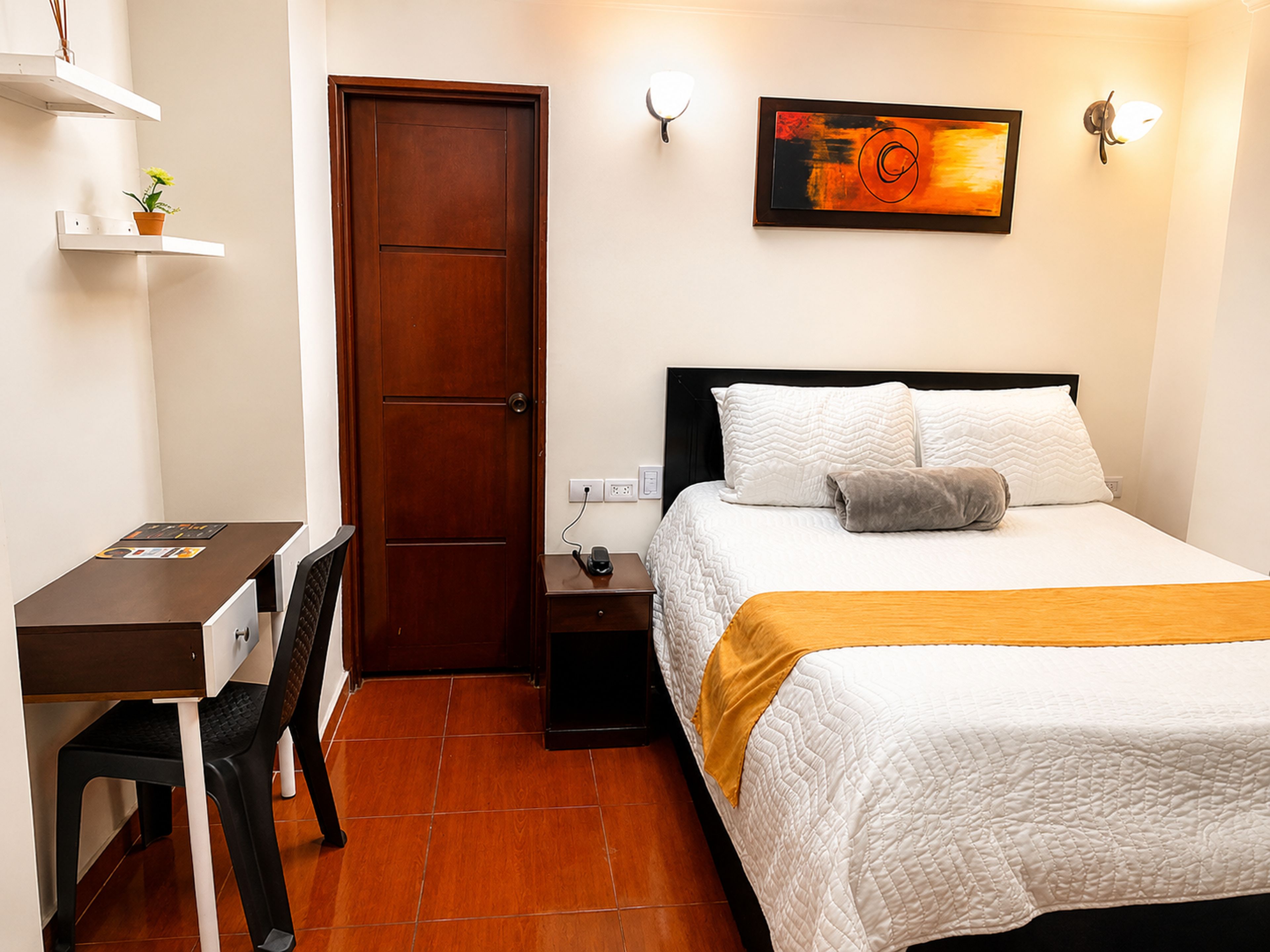 Una habitación de hotel con cama, mesita de noche, silla, escritorio y una puerta.