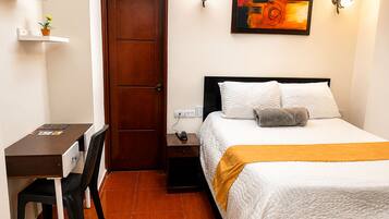 Una habitación de hotel con cama, mesita de noche, silla, escritorio y una puerta.
