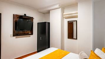 Una habitación de hotel con una cama, un armario, un televisor montado en la pared y un equipo de aire acondicionado.