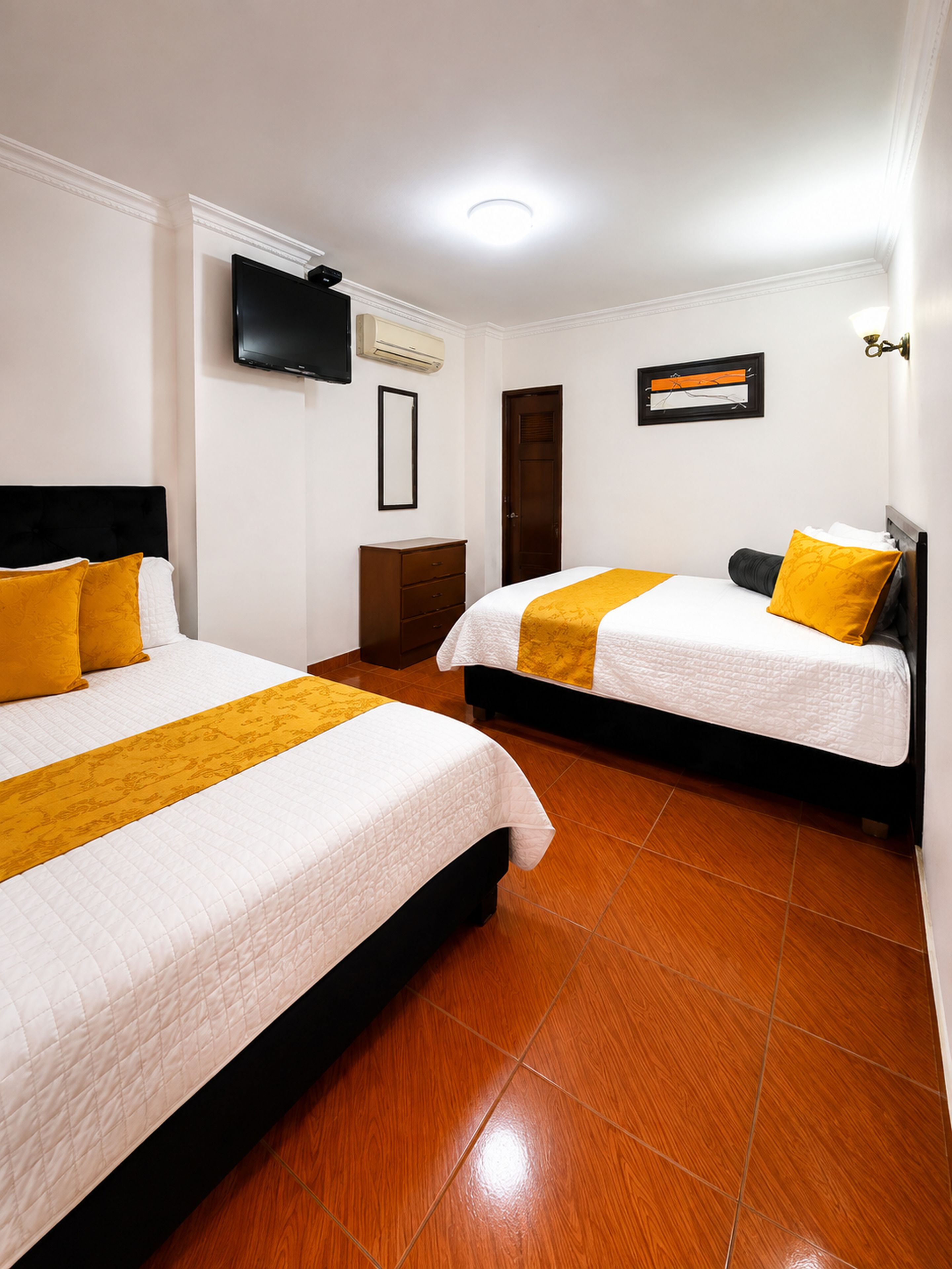 Habitación de hotel con dos camas, un televisor de pantalla plana, un equipo de aire acondicionado y un cuadro en la pared.