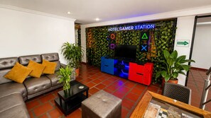 A hotel lobby with a leather sofa, a coffee table, and a gaming station with a TV and drawers. - Hotel Avenida 3 Real (Cali)
