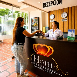 Una recepción de hotel con un reloj que muestra la hora de Nueva York, un letrero que indica el área de recepción y el logotipo del hotel.