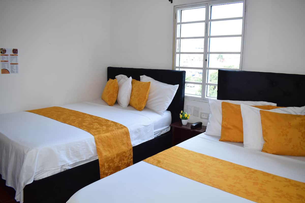 A hotel room with two beds, each with white bedding and yellow accents, a window with a view, and a small table with a vase of flowers.