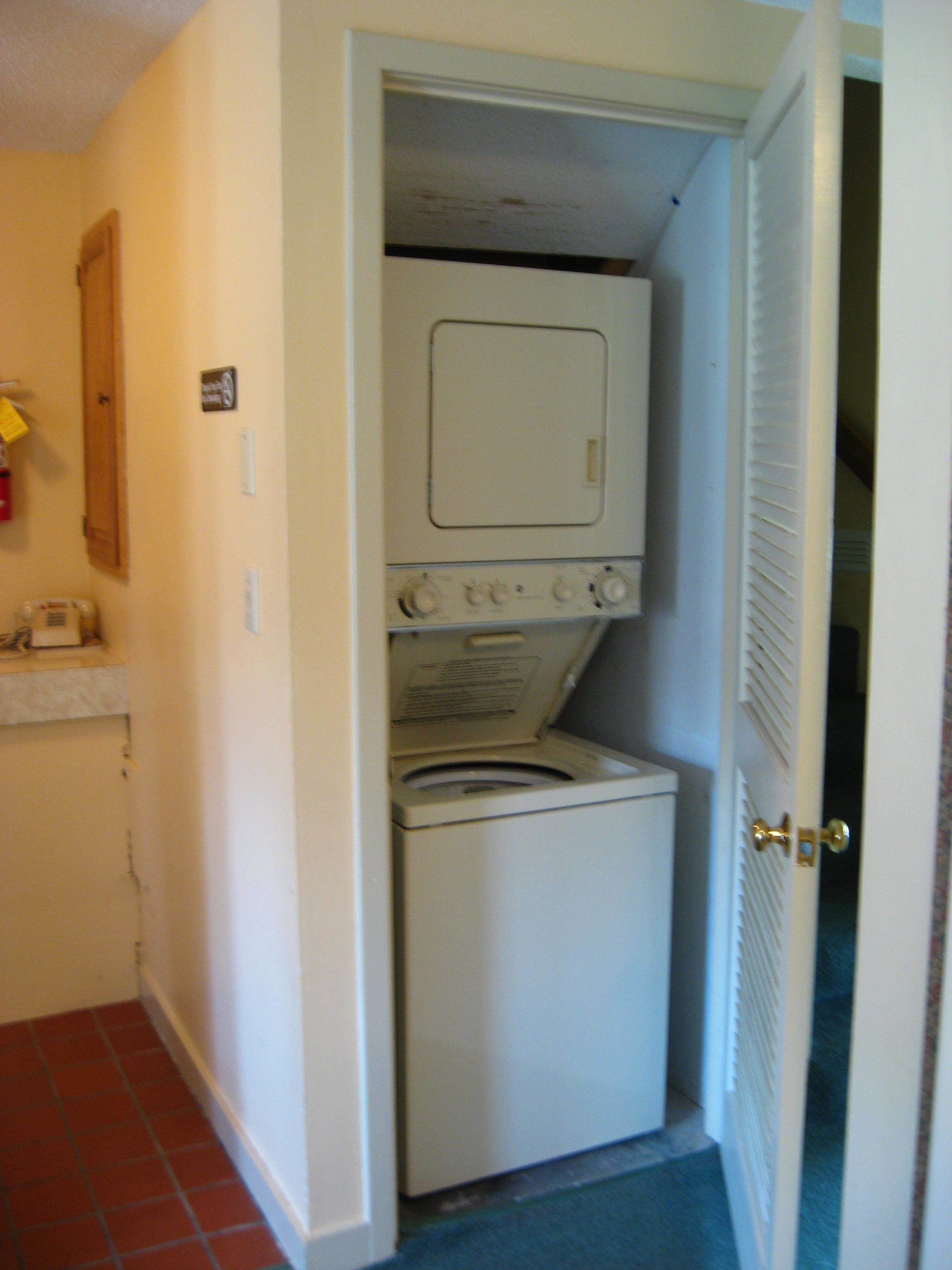 Une buanderie équipée d’un lave-linge et d’un sèche-linge, avec une porte en bois et un sol carrelé.