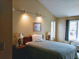 Un dormitorio con una cama, dos lámparas de noche, un cuadro enmarcado en la pared y un ventanal con cortinas.